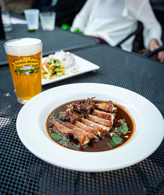 Bowl of sliced tuna pepper steak and oxtail with side of crunchy veggies and glass of beer.