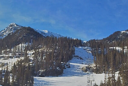 A wide ski run with a lift at the base on a sunny day.