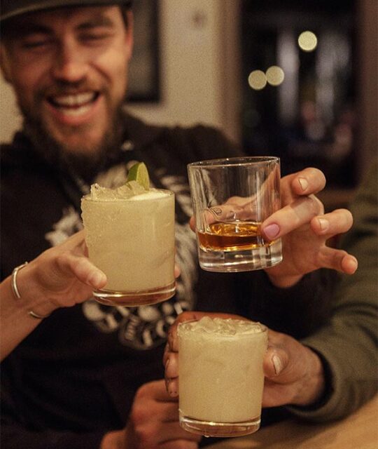 Three friends raising their cocktails for a toast at ACEQ.