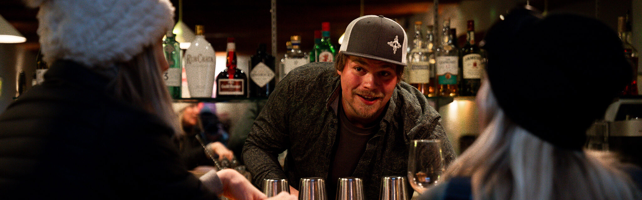 A bartender looks up at two customers and smiles while chatting.