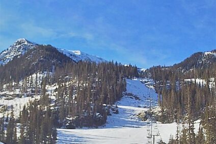 A wide ski run with a lift at the base on a sunny day.