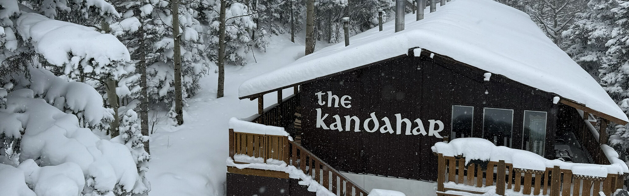 The Kandahar lodge sits quietly with a thick blankets of snow, surrounded by tall trees.