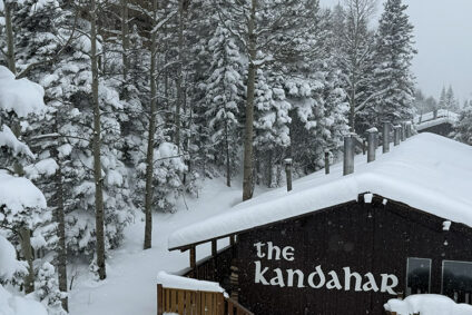 The Kandahar lodge sits quietly with a thick blankets of snow, surrounded by tall trees.