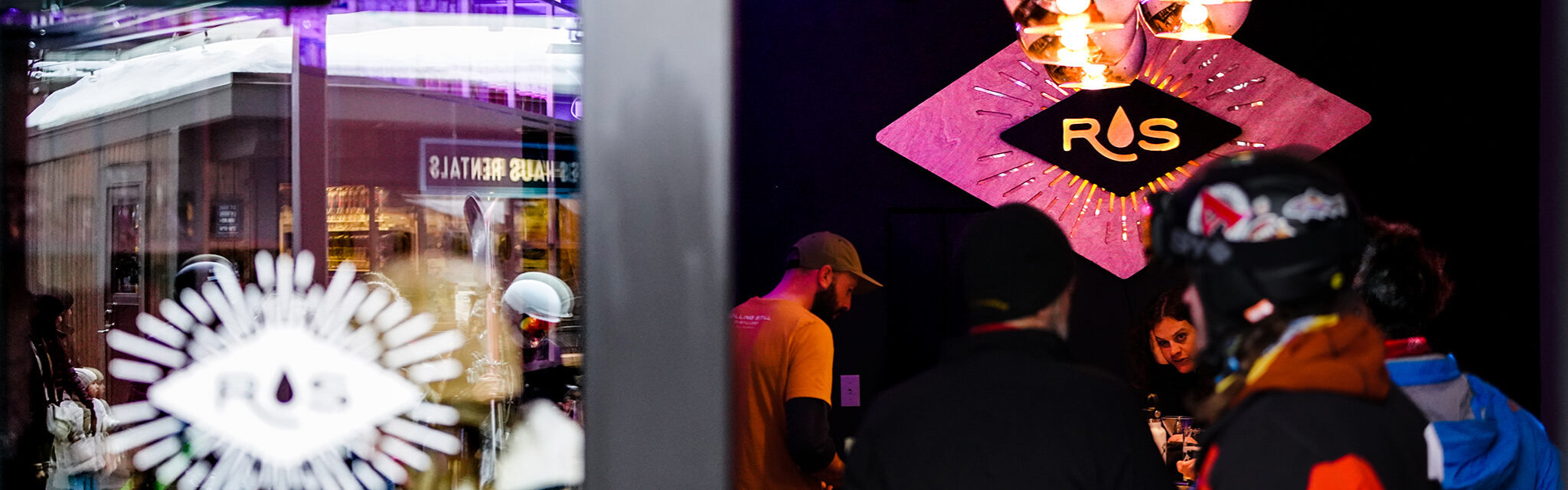A woman with dark hair catches the camera's eye across a dark, busy bar.