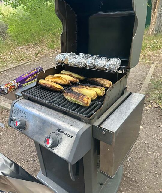 Corn of the cob and baked potatoes on an outdoor grill.