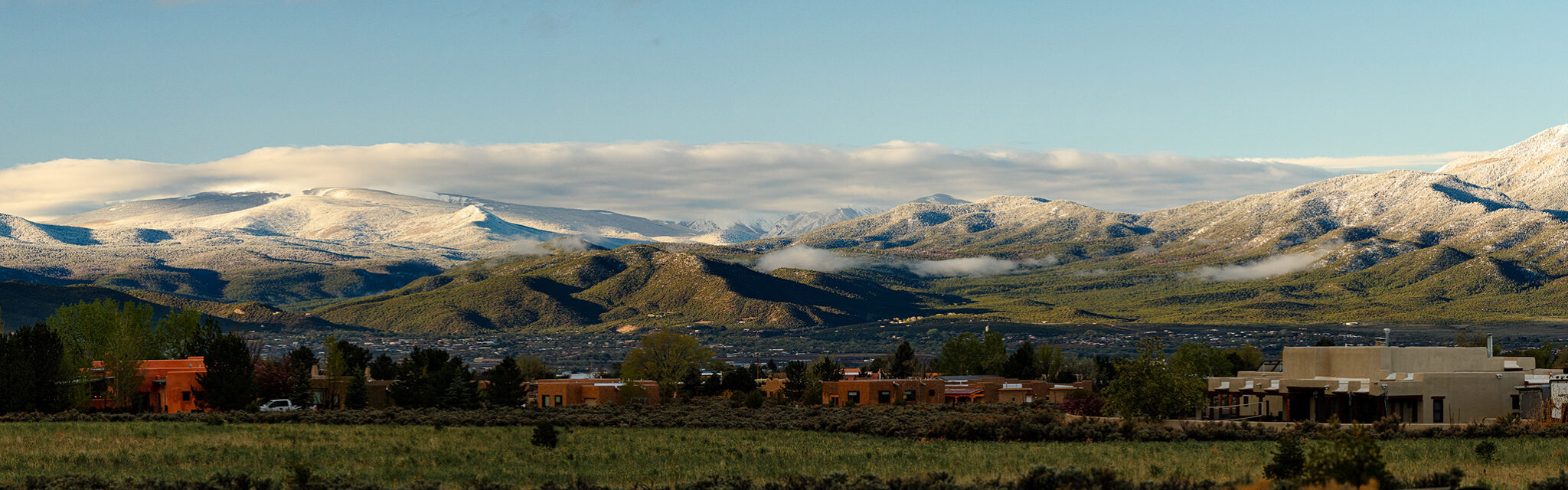 Snow capped mountains sit behind a verdant valley below.
