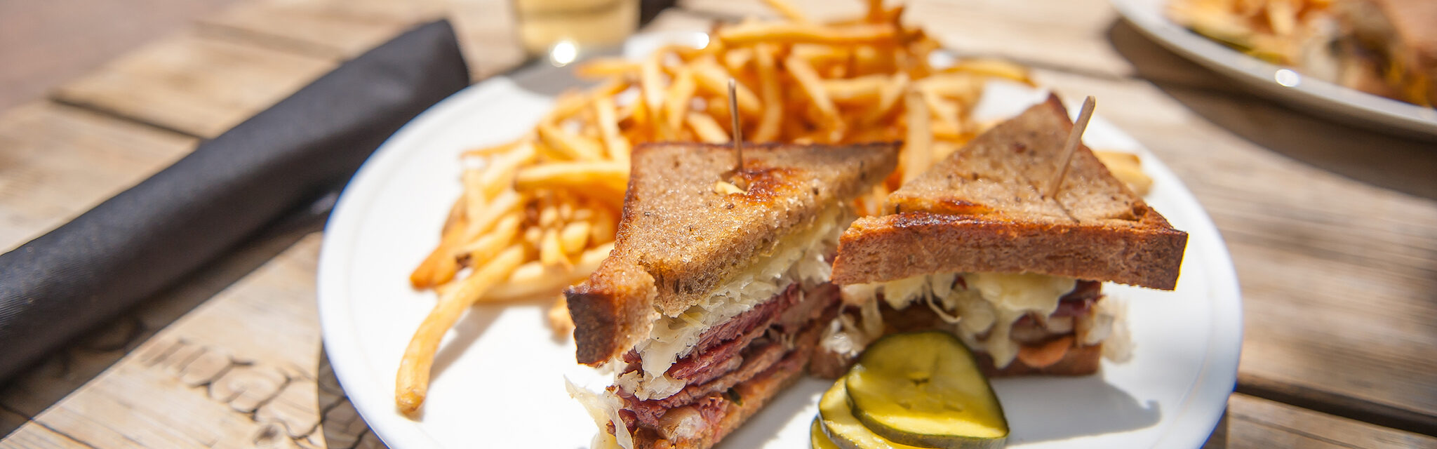 A reuben sandwich with fries and homemade pickles on a plate at an outdoor patio.