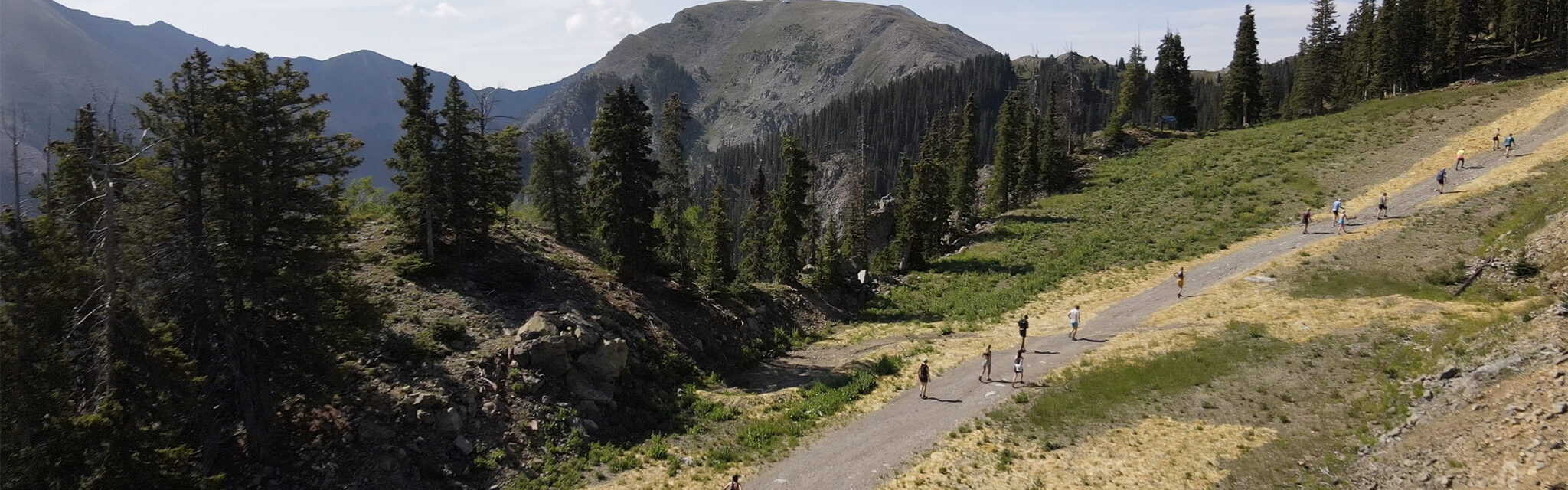 An aerial image of runners heading uphill on a dirt road with a large mountain in the distance.