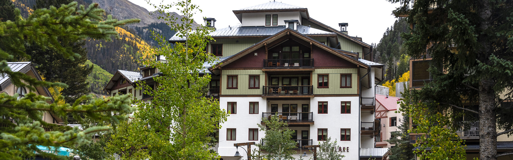 A four story hotel sits in a mountain valley with yellow, fall trees.