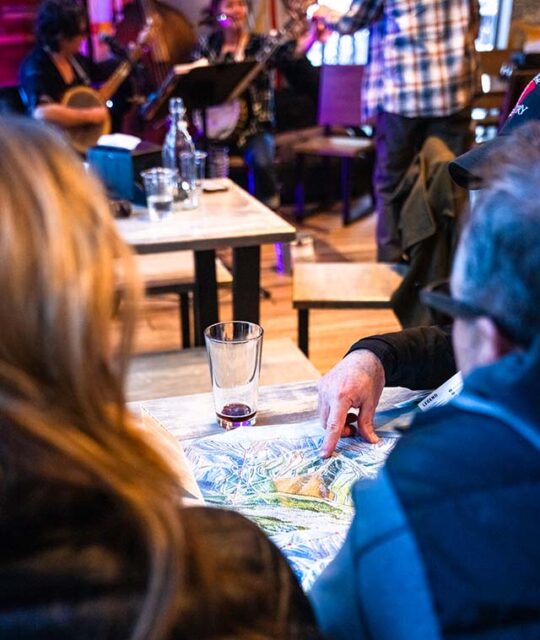 Musicians play in the background while guest look over a ski trail map at DALEEE TSV.