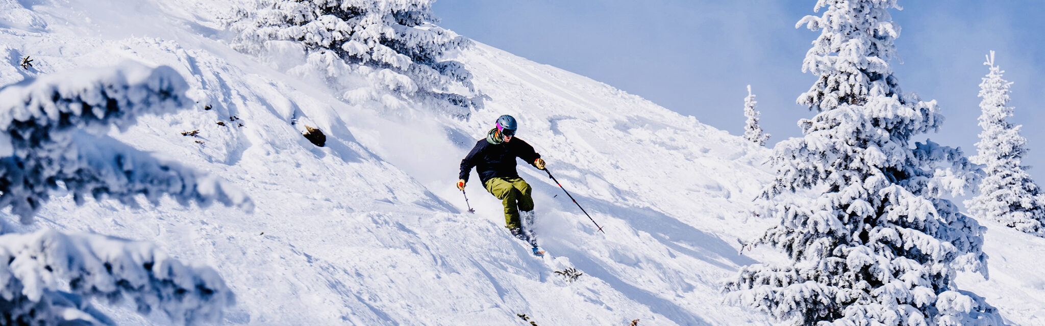 A solo skier comes down a hill in powder with blue skies.