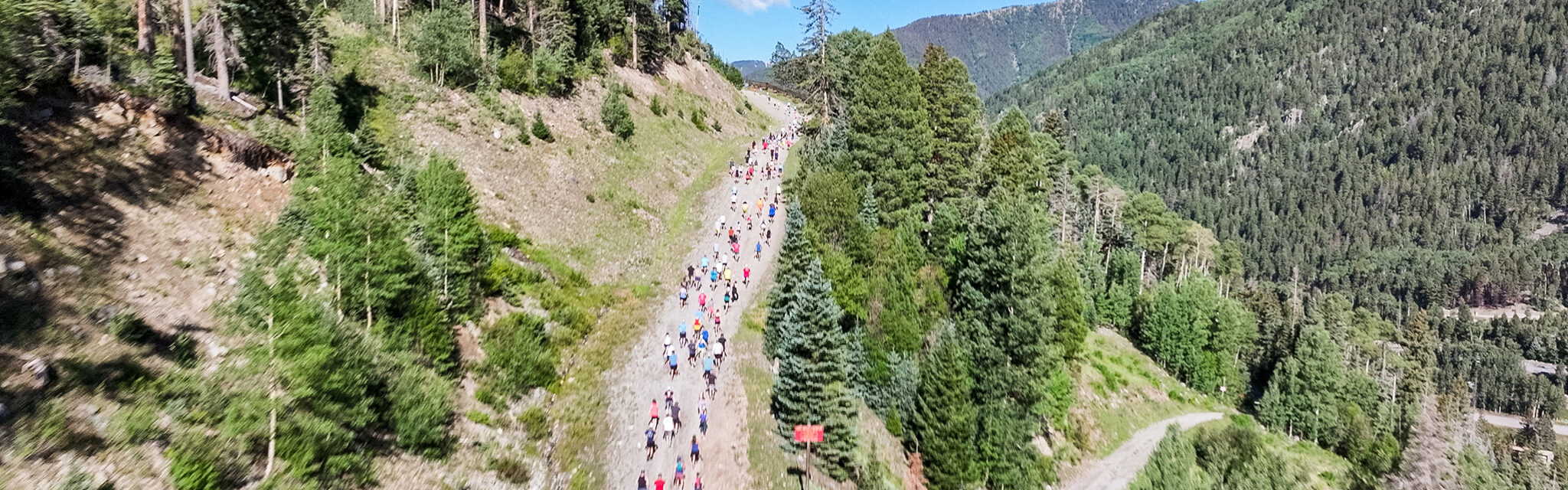 A group of runners head up a dirt road on the side of a mountain.