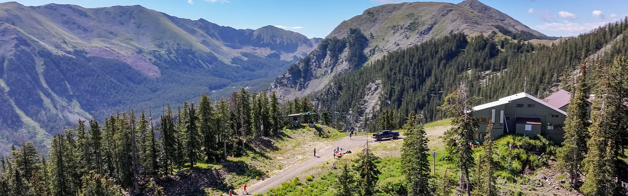 A wide view of bare mountain peaks with runners on a dirt road in the foreground.