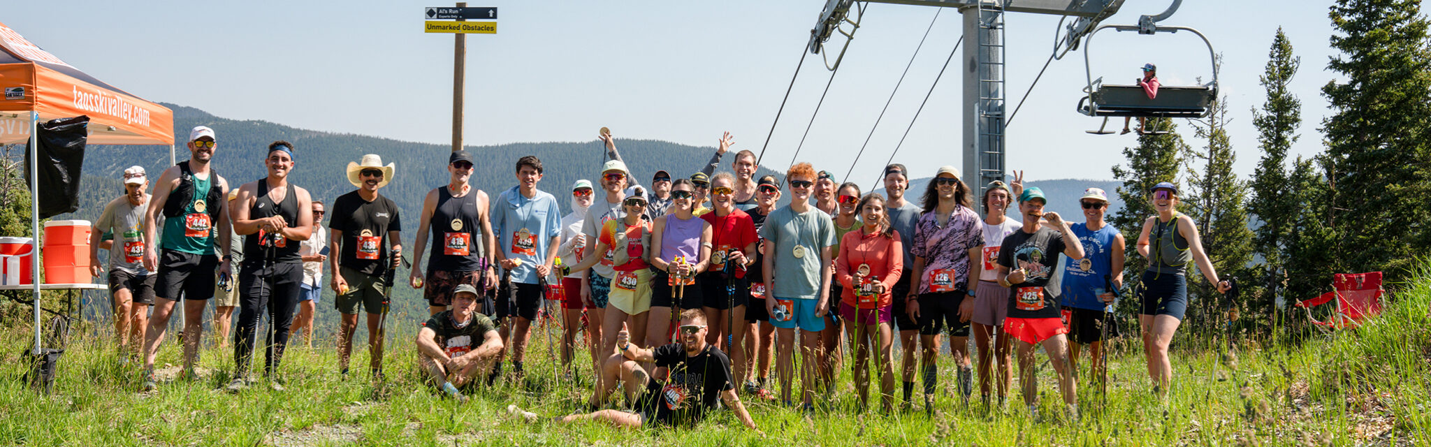A line of runners pose at the top of a hill after a race with a ski lift in the background.