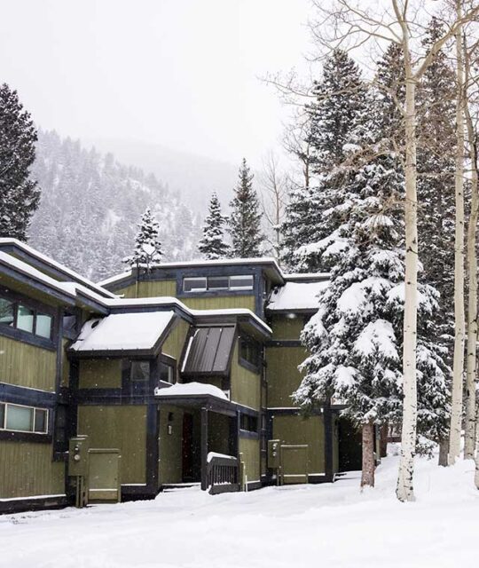 Exterior of the Rio Hondo Condo at Taos Ski Valley after a powder day with surrounding aspen trees.