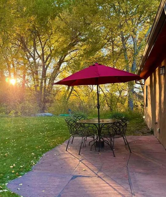 Table with red umbrella seating overlooking a beautiful green lawn and sunset coming through the trees.