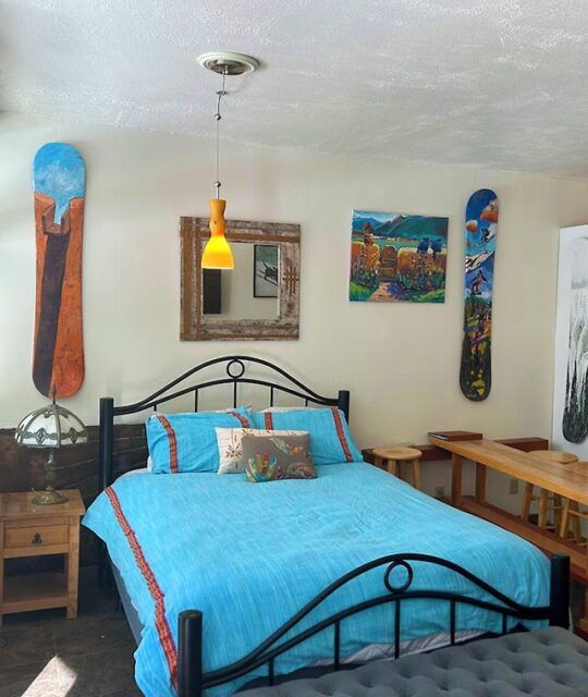 Queen bed with blue comforter and painted snowboards on the wall.