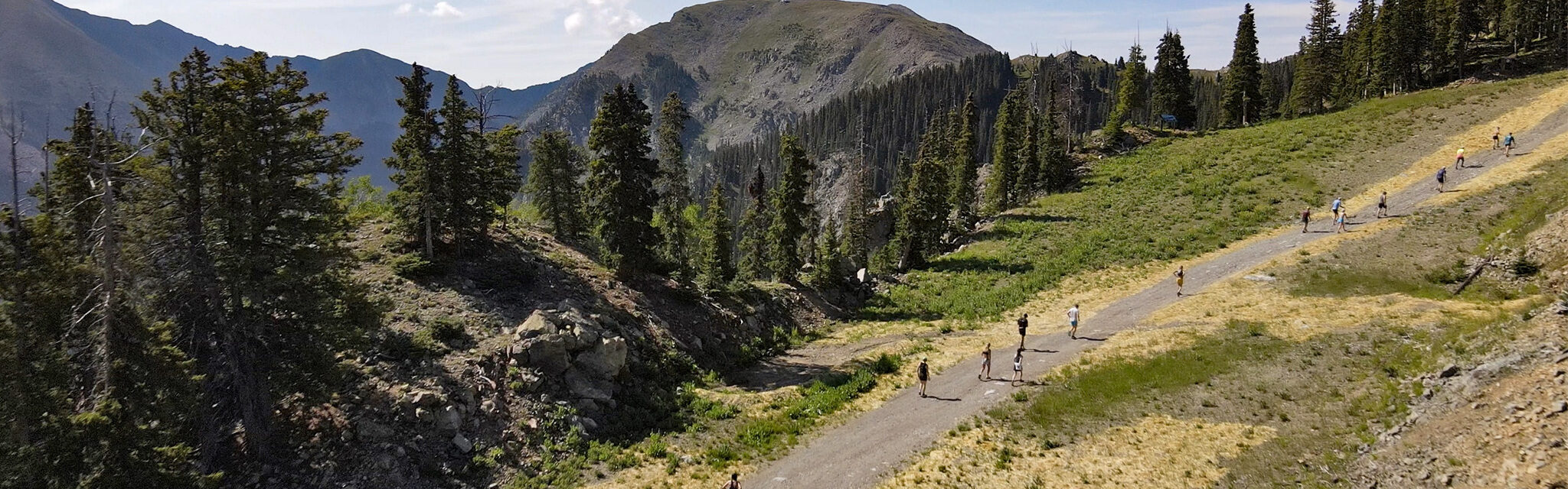 An aerial image of runners heading uphill on a dirt road with a large mountain in the distance.